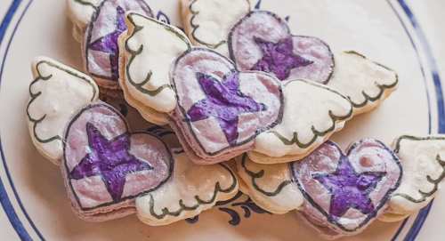 A plate of heart-shaped cookies with purple stars and white wings, decorated with colorful icing.