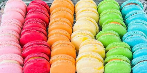 A colorful array of macarons in pink, red, orange, yellow, green, and blue, neatly arranged in rows.