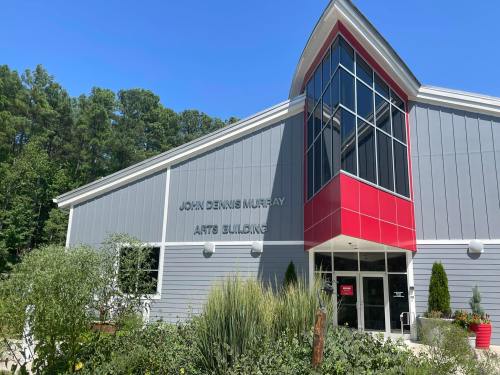 Exterior of the John Dennis Murray Arts Building, featuring modern architecture and greenery under a clear blue sky.