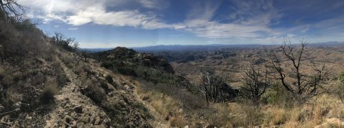 Panoramic view of a rugged landscape with dry hills, sparse vegetation, and a blue sky with scattered clouds.