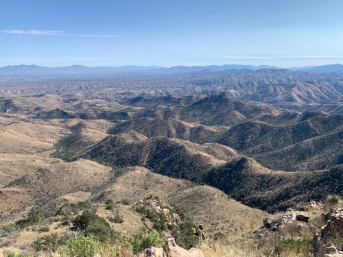 A panoramic view of rolling hills and mountains under a clear blue sky, showcasing a vast, arid landscape.