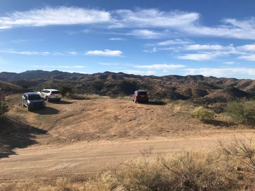 Three cars parked on a dirt road with a mountainous landscape and blue sky in the background.