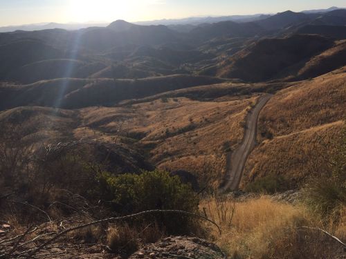 A scenic view of rolling hills and a winding dirt road under a bright sky, with sunlight illuminating the landscape.