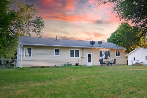 A single-story house with a grassy yard, surrounded by trees, under a colorful sunset sky.
