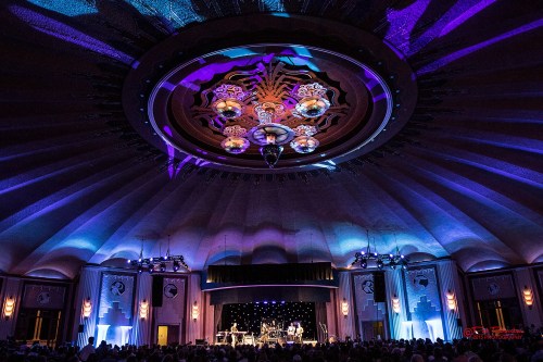 A vibrant concert scene with colorful lighting, featuring a stage and a beautifully designed ceiling.