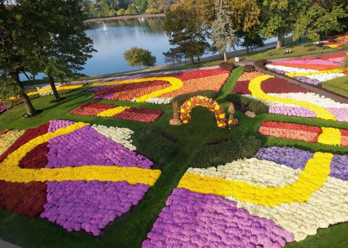 Aerial view of a vibrant flower garden with colorful patterns and a small archway near a serene lake.