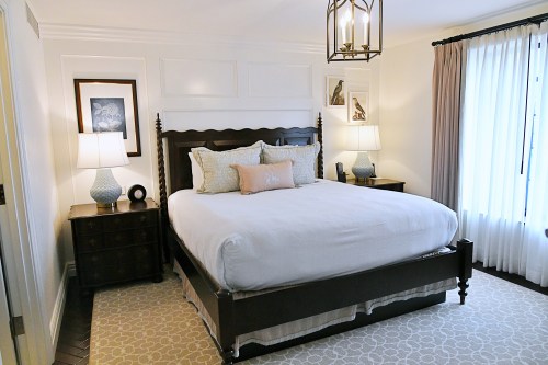 A cozy bedroom featuring a large bed, two bedside lamps, and elegant decor with light curtains and a patterned rug.