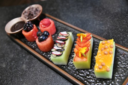 A colorful dessert platter featuring fruit and decorative toppings on a dark stone surface.