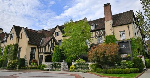 A charming Tudor-style building with lush greenery and a sign for a hotel, set against a cloudy sky.