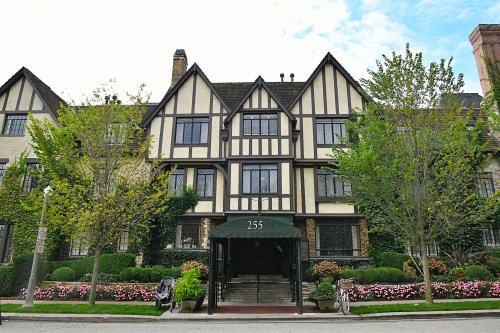 Tudor-style building with a green awning, surrounded by trees and colorful flower beds.