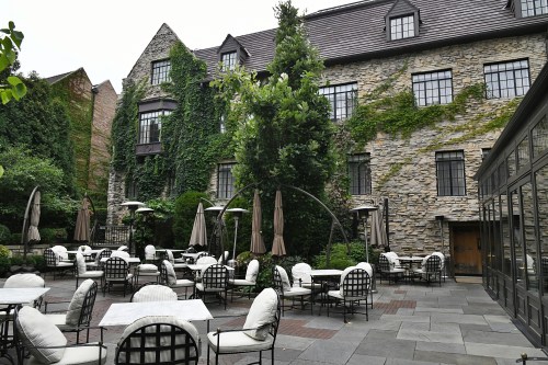 A charming outdoor patio with stone walls, lush greenery, and tables set for dining.