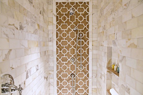 A modern shower with a decorative tile design, featuring marble walls and a sleek showerhead.