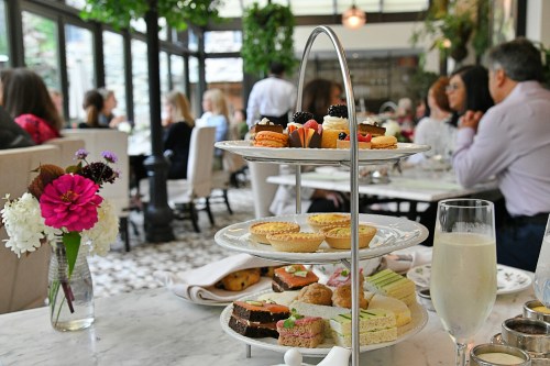 A tiered stand of assorted pastries and desserts in a café setting, with guests enjoying their time in the background.