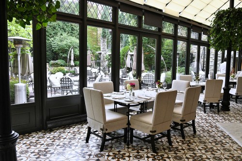 A bright dining area with elegant chairs and tables, overlooking a lush garden through large glass windows.