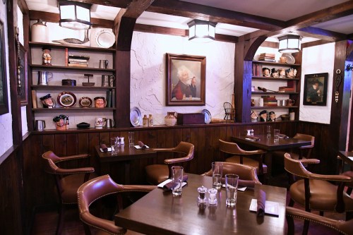 Cozy restaurant interior with wooden beams, shelves of decor, and tables set for dining. Warm, inviting atmosphere.