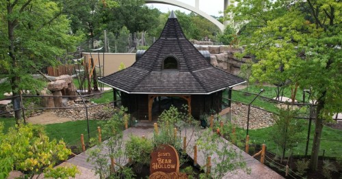 A scenic view of a wooden structure surrounded by greenery and rocks, labeled "Susi's Bear Hollow."