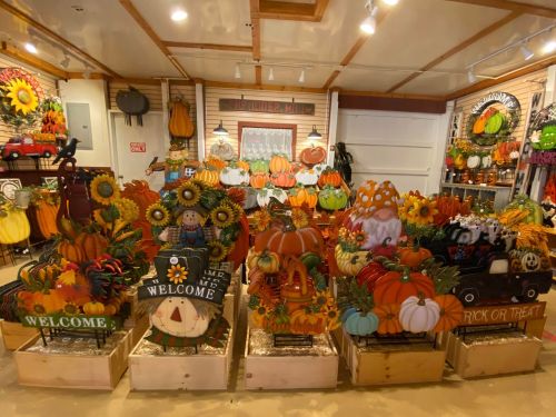 A vibrant display of autumn decorations, including pumpkins, scarecrows, and welcome signs, in a cozy shop setting.