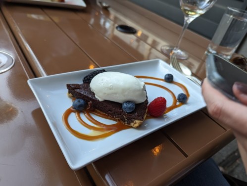 A chocolate dessert topped with vanilla ice cream, garnished with berries and drizzled with caramel sauce on a white plate.