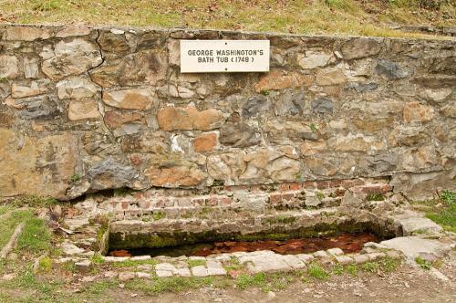 A stone structure with a sign reading "George Washington's Bath Tub (1748)" above a shallow, water-filled trough.