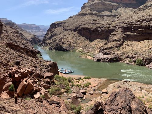 A scenic view of a river winding through rocky canyons, with a small beach and boats along the shore under a clear sky.