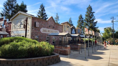 A sunny view of a rustic building facade with signs, surrounded by trees and a pathway.