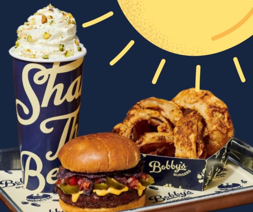 A burger with toppings, onion rings, and a milkshake topped with whipped cream and nuts, set against a sunny background.
