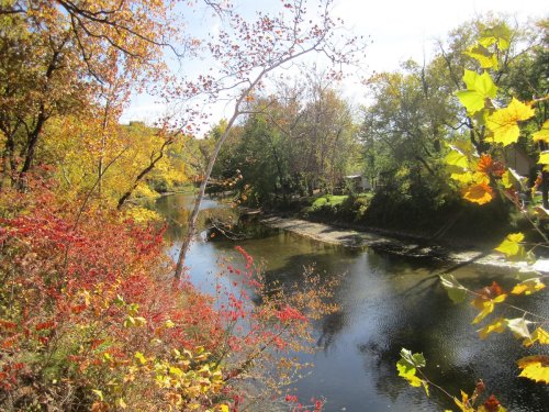 A serene river scene surrounded by vibrant autumn foliage and trees reflecting in the water under a clear blue sky.