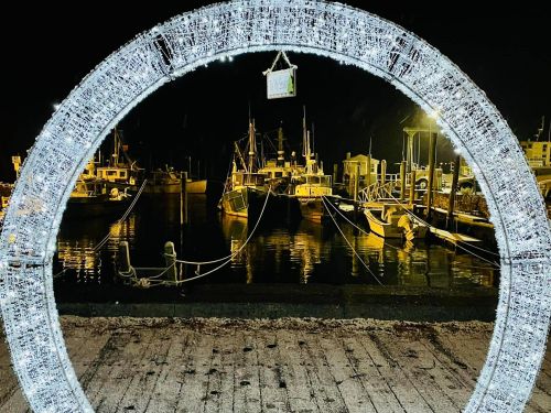 A circular light frame at night, overlooking a harbor filled with illuminated boats and reflections on the water.