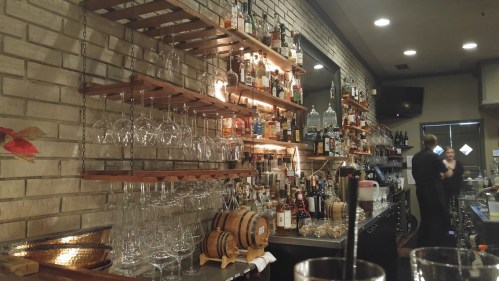 A cozy bar with shelves of liquor bottles, hanging glasses, and a bartender preparing drinks in a warm atmosphere.