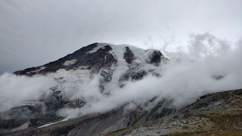 A mountain peak partially obscured by clouds and mist, with rocky terrain in the foreground.