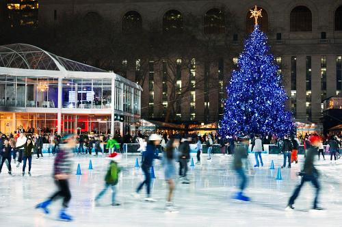 A bustling ice skating rink with a large blue Christmas tree and people skating in a festive atmosphere.