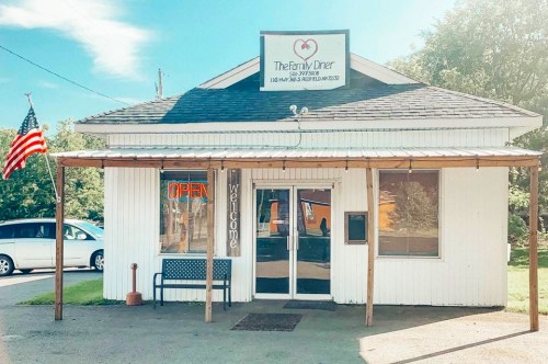 A small diner with a sign reading "The Family Diner," featuring an open flag and a bench outside.