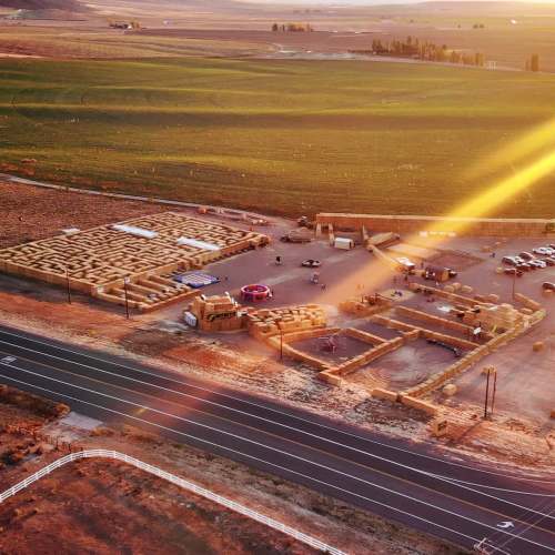 Aerial view of a maze and parking area in a rural landscape during sunset, with fields and distant hills.