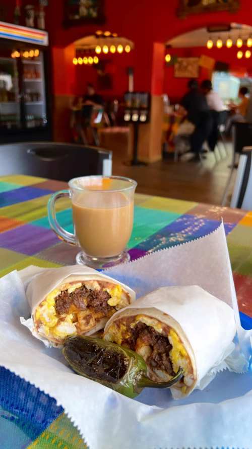 A close-up of a burrito with beef and eggs, served with a jalapeño and a cup of coffee in a colorful restaurant setting.