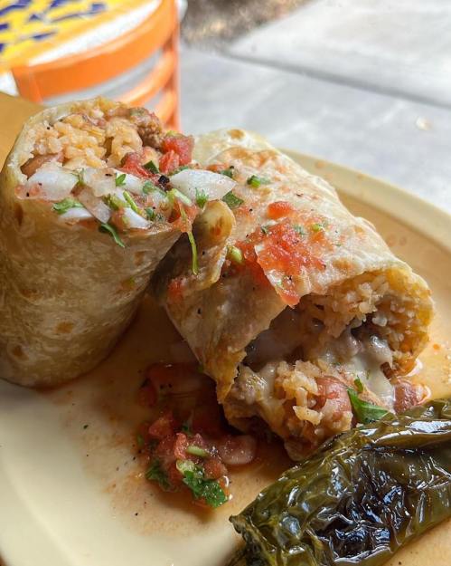 A close-up of a burrito filled with rice, meat, and salsa, served with a green chili on a plate.