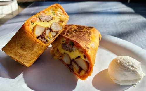 A close-up of a cut burrito filled with potatoes, eggs, and meat, served on a plate with a scoop of ice cream.