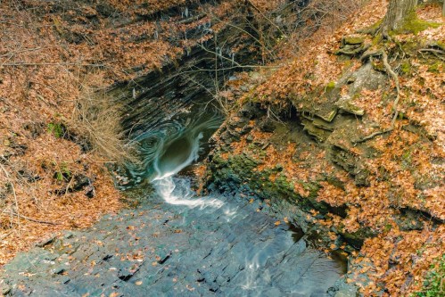 A serene waterfall cascades over rocky terrain, surrounded by autumn leaves and bare trees.