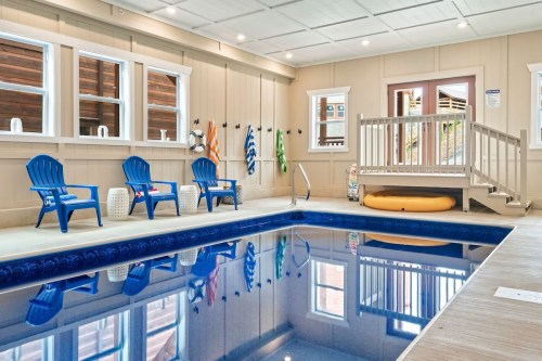 Indoor pool area featuring blue chairs, a lifebuoy, and a slide, with large windows and wooden accents.