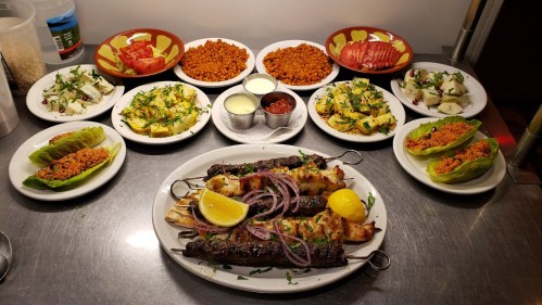 A spread of various dishes including skewers, salads, and dips, arranged on plates with vibrant colors and garnishes.