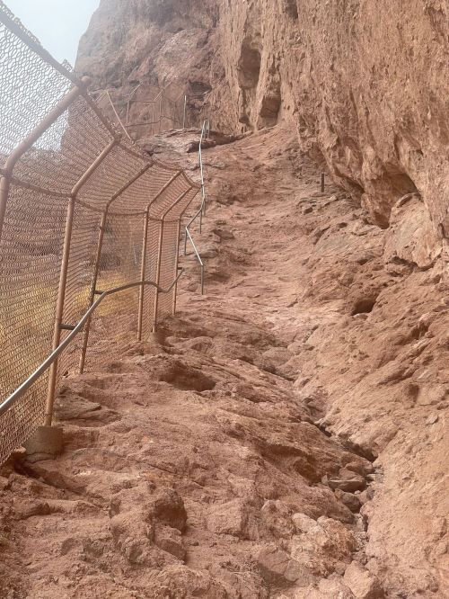 A rocky, steep path with a metal fence and railing, leading up a mountain or cliffside.