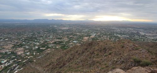 A panoramic view of a valley with scattered houses and mountains under a cloudy sky at sunset.