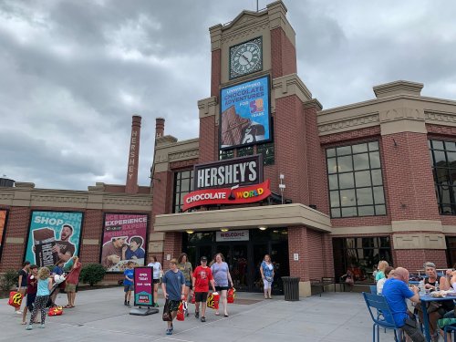 Exterior of Hershey's Chocolate World with visitors, featuring a large clock and colorful advertisements.