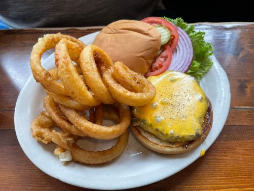 A plate with a cheeseburger topped with lettuce, tomato, and onion, alongside crispy onion rings.