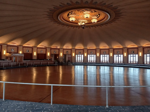 A spacious, elegantly designed hall with a circular wooden floor and ornate ceiling lights.