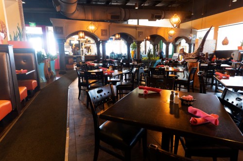 Interior of a restaurant featuring dark wooden tables, black chairs, and colorful decor with pink napkins on the tables.