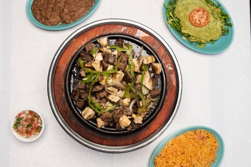 Sizzling beef and cheese fajitas served on a skillet, surrounded by sides of rice, guacamole, beans, and salad.