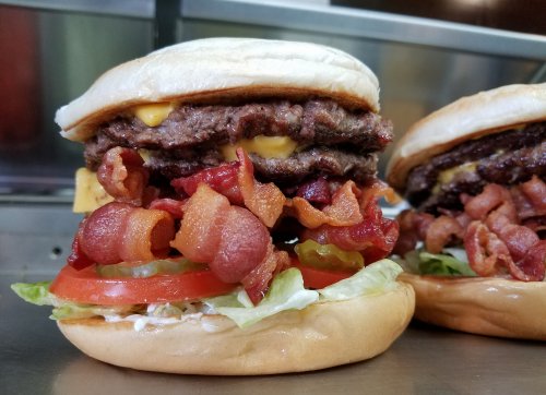 A close-up of a double cheeseburger with bacon, lettuce, tomato, and mayonnaise on a toasted bun.
