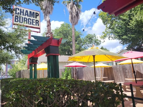 Outdoor seating area at Champ Burger, featuring colorful umbrellas and lush greenery under a bright blue sky.