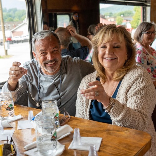 Two smiling people sitting at a table in a cozy restaurant, enjoying a meal with others in the background.