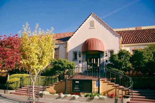 Historic building with a brown awning, surrounded by trees and colorful landscaping under a clear blue sky.